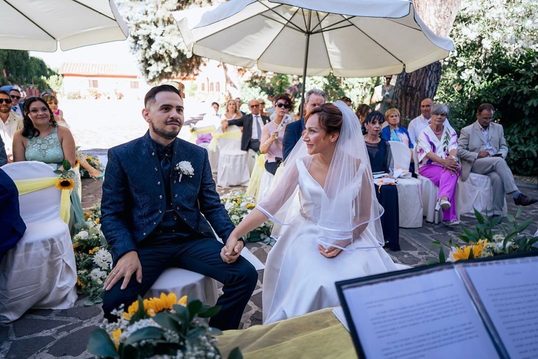 Gli sposi seduti durante la cerimonia nei giardini di Villa Dafne Majestic, con gli invitati intorno Gli sposi seduti durante la cerimonia nei giardini di Villa Dafne Majestic, con gli invitati intorno